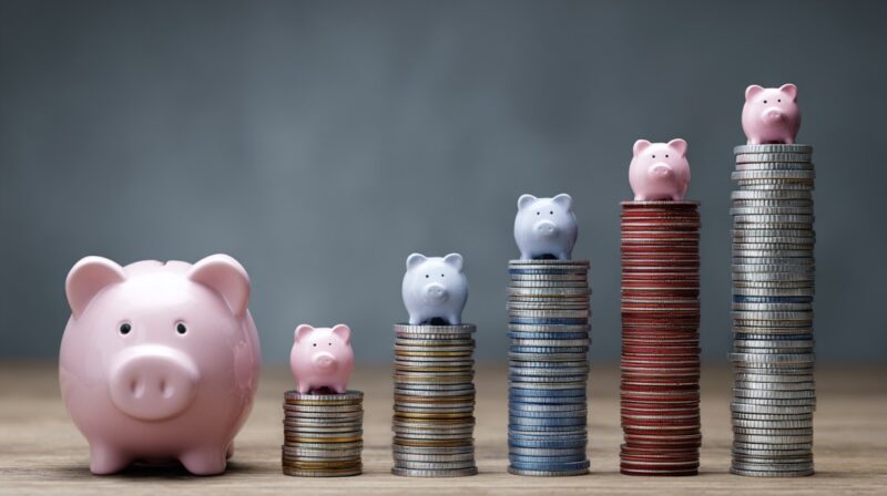 Piggy banks of different sizes placed on stacks of coins, symbolizing varying financial costs