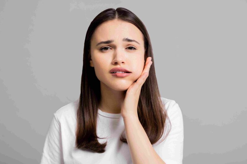 Woman holding her jaw while experiencing ongoing tooth pain and discomfort